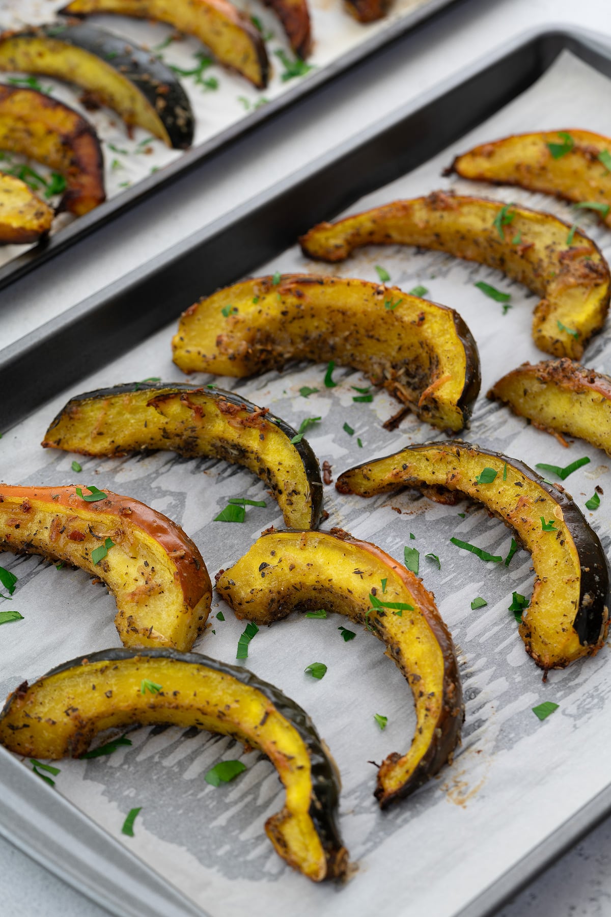Slices of roasted acorn squash in a baking tray, presented on a white table.
