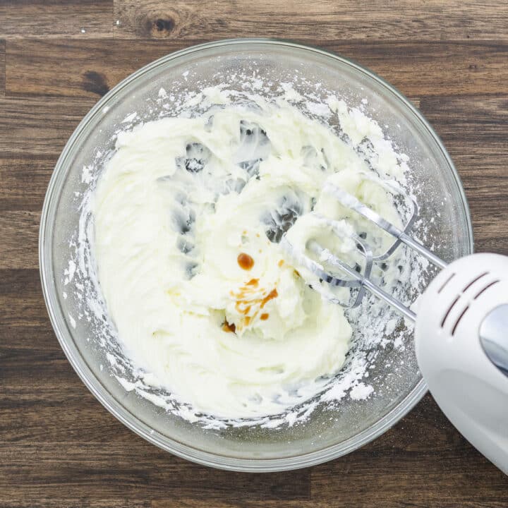 Bowl containing creamed butter with vanilla extract, mixed with an electric beater.