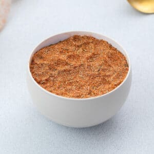 Steak seasoning mix displayed in a white bowl, set on a white table.