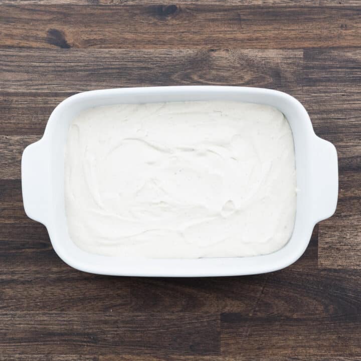 A shallow baking tray featuring a creamy base of taco dip.