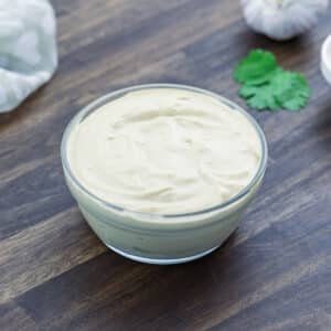 Tahini sauce served in a glass bowl with coriander leaves and a towel on the side.