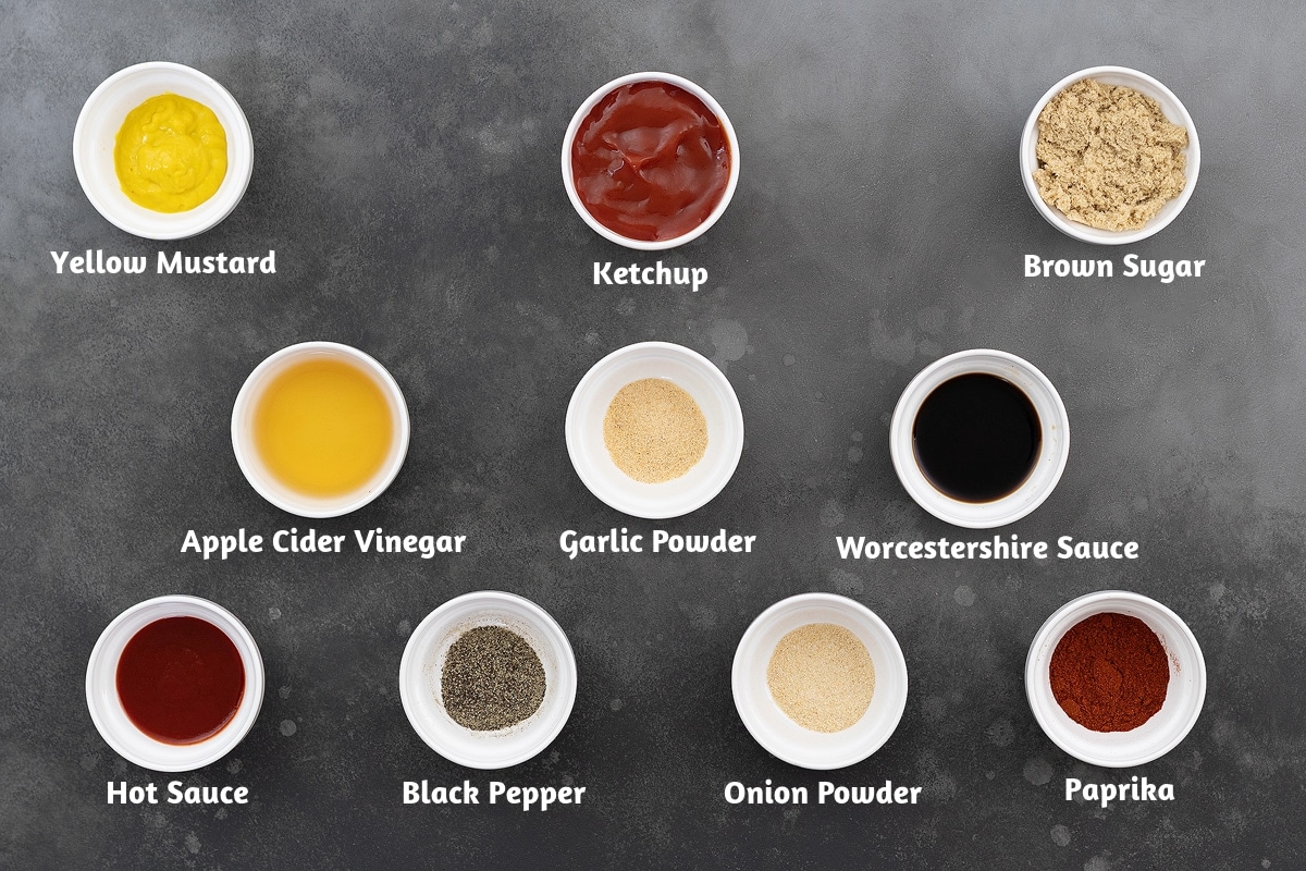 Ingredients for BBQ sauce arranged on a grey table: Yellow Mustard, Ketchup, Brown Sugar, Apple Cider Vinegar, Garlic Powder, Worcestershire Sauce, Hot Sauce, Black Pepper Powder, Onion Powder, Paprika.