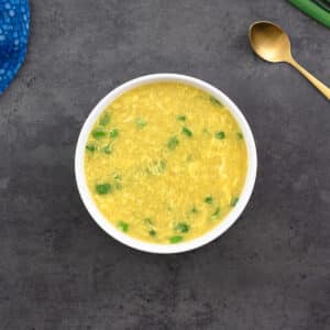 Egg Drop Soup elegantly served in a white bowl, accompanied by a golden spoon, creating a visually appealing presentation.