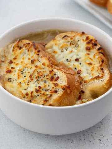 Homemade French onion soup served in a white bowl, garnished with crusty bread on top.