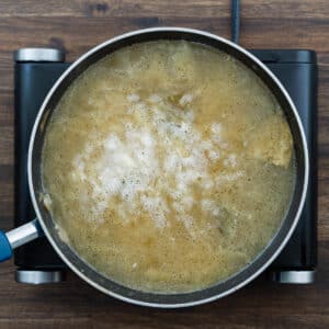 Onions simmering in broth on a stovetop pan.