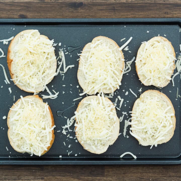 A baking tray displaying crusty bread topped with cheese.
