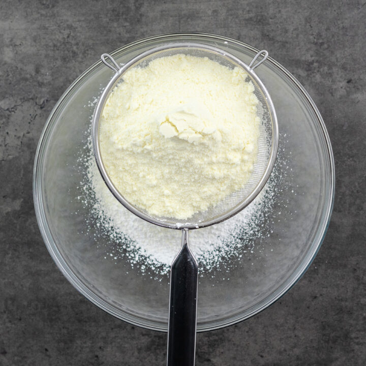 A bowl with sifted powdered sugar and a mesh strainer on top, containing milk powder.