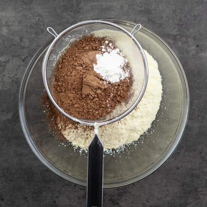 A mesh strainer with cocoa powder and cornstarch on top of a bowl for sifting.