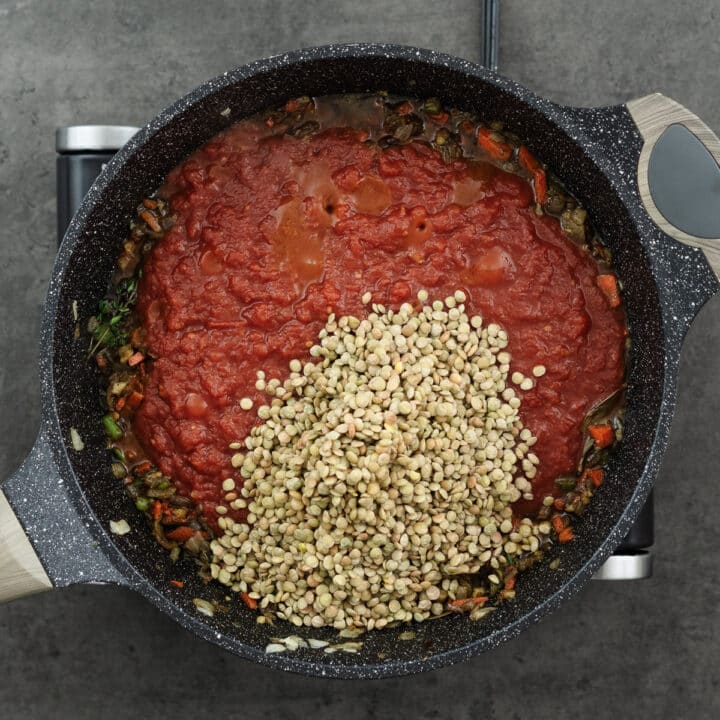 A pan featuring seasoned veggies, crushed tomatoes, and lentils for a rich and hearty soup mixture.