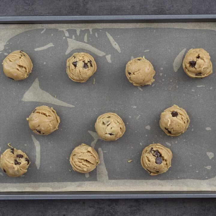 Portioned peanut butter chocolate chip cookie dough arranged on a baking tray lined with parchment paper.