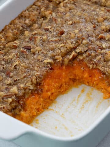 Sweet potato casserole in a white baking dish on a table, with a slice taken out.