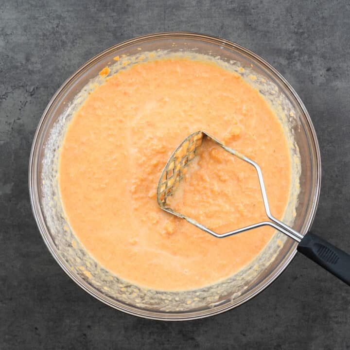 Bowl with sweet potato casserole mix, showcasing a masher for preparation.