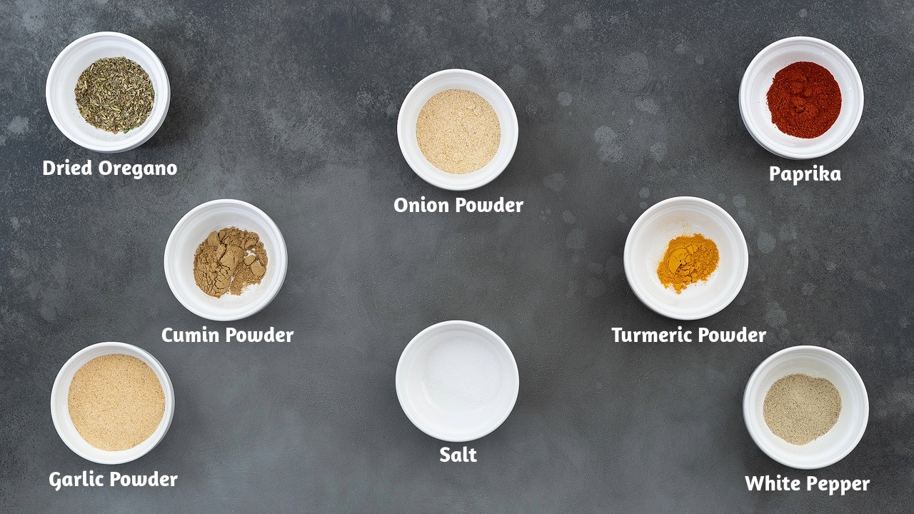 Ingredients for adobo seasoning, including dried oregano, onion powder, paprika, cumin powder, turmeric powder, garlic powder, salt, and white pepper, arranged on a gray table.