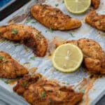 Baked chicken tenders on a tray, garnished with fresh cilantro and lemon slices.