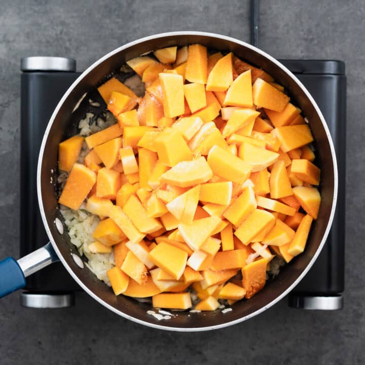 A pan with chopped squash seasoned with salt, alongside aromatics.