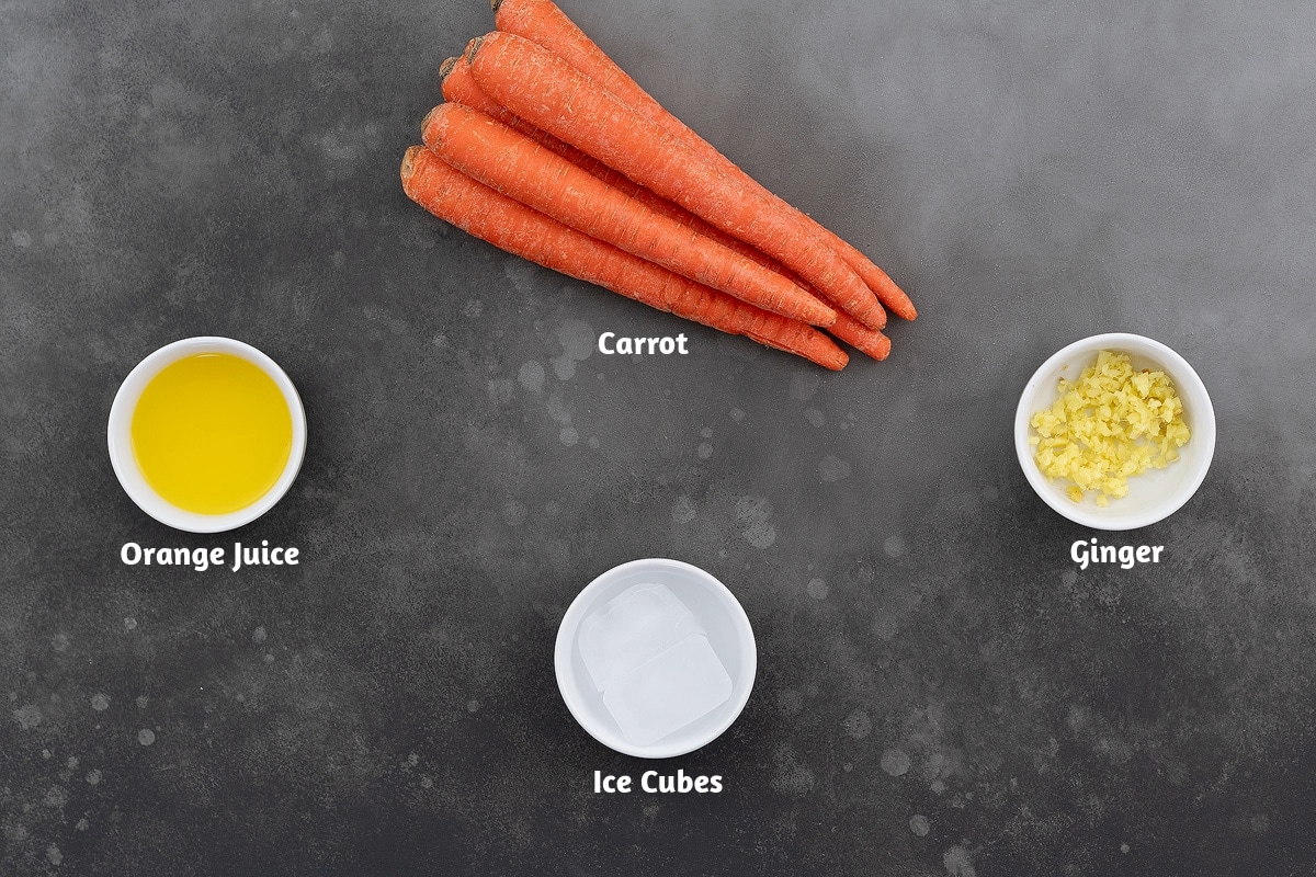 Ingredients for making carrot juice, including carrots, orange juice with ginger, and ice cubes, arranged on a gray table.