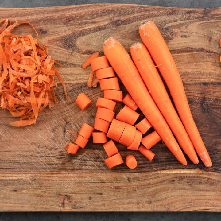 A cutting board with peeled and chopped carrots, with carrot peels on the side.