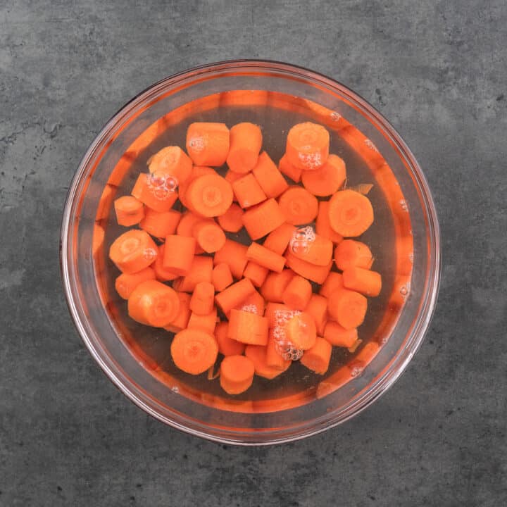 A bowl containing carrots soaking in warm water.
