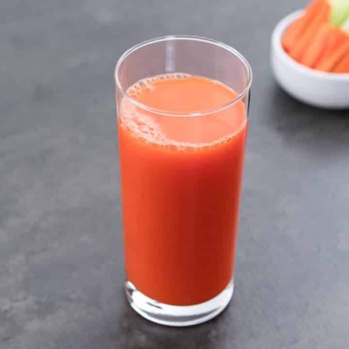 Carrot juice served in a glass, accompanied by fresh carrot pieces on the side.