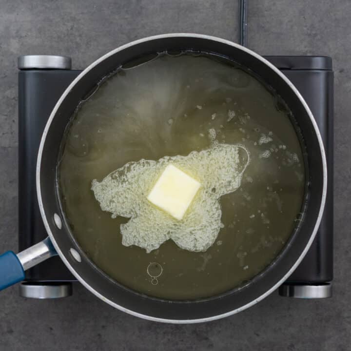 Wide-bottomed pan containing broth and butter.