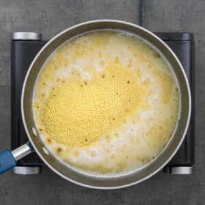 Wide-bottomed pan filled with couscous in broth mixture.