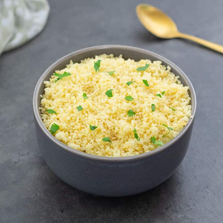Grey bowl filled with couscous, garnished with cilantro leaves.