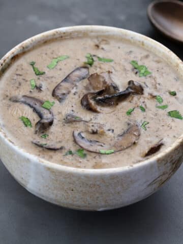 Cream of mushroom soup in a cup on a gray table, with a wooden spoon.