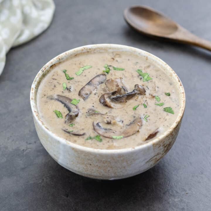 Cream of mushroom soup served in a ceramic bowl, garnished with parsley leaves.