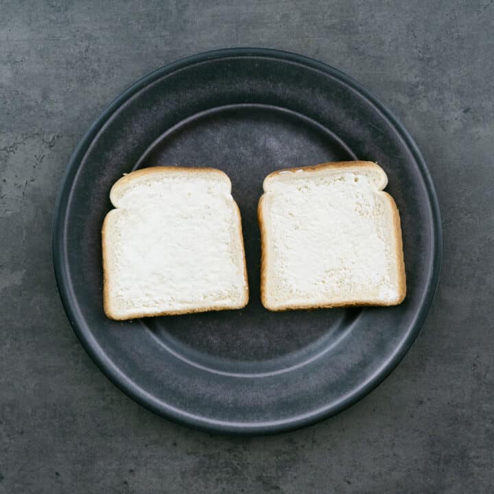 Two bread slices on a plate, one side spread with butter.