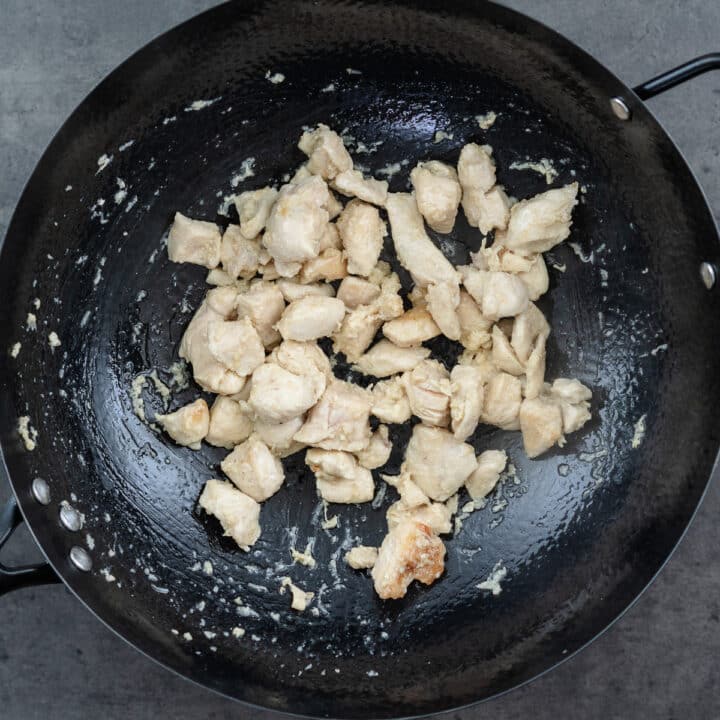 A wok with marinated chicken cooked to white in color.