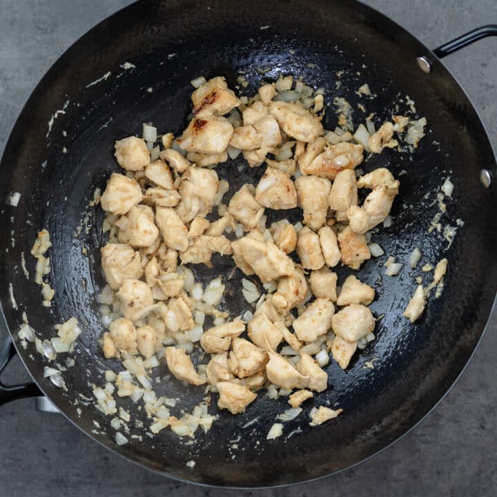 A wok with cooked chicken and onion.