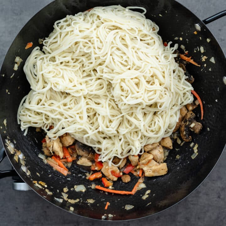 A wok with cooked chicken, veggies, sauces, and noodles.