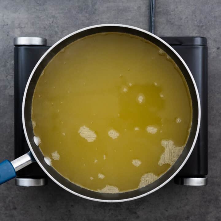 Chicken broth simmering in a wide-bottom pan over medium heat on the stove.