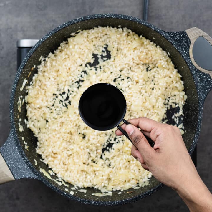White wine being poured into the pan with rice and stirred until absorbed.