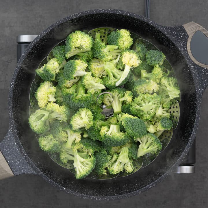 A pan featuring a steamer basket filled with broccoli florets enveloped in steam.