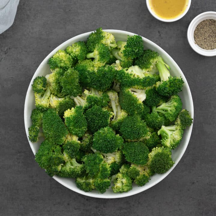 A white plate showcasing perfectly steamed broccoli, seasoned with a dash of salt and black pepper.