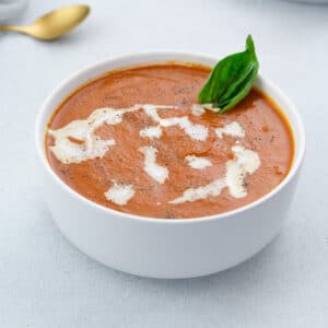 Creamy tomato soup served in a white bowl on a white table, accompanied by a golden fork nearby.