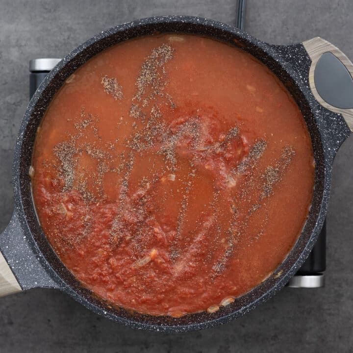 Tomato soup mixture seasoned with black pepper and salt in a pan.