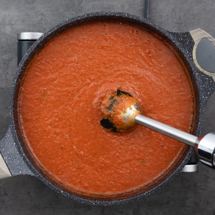 Tomato soup mixture being blended with an immersion blender in a pan.