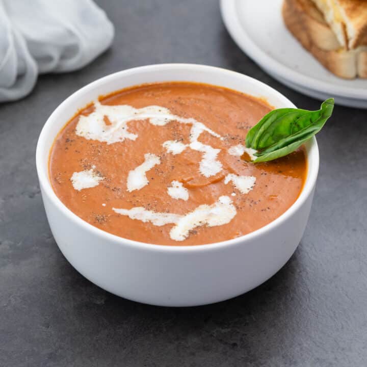 Creamy Tomato Soup served in a white bowl, topped with heavy whipping cream and basil leaves.