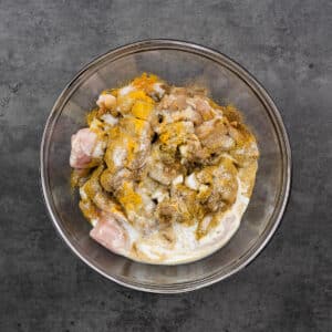 Bowl with chicken thighs, spices, and coconut milk mixture.