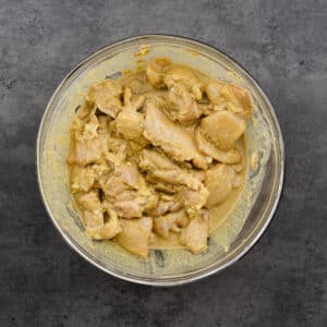 Bowl with chicken marinating in satay marinade.