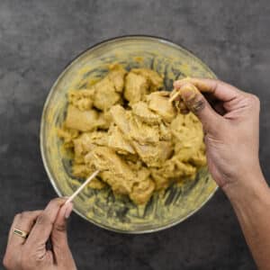 Threading marinated chicken onto skewers.