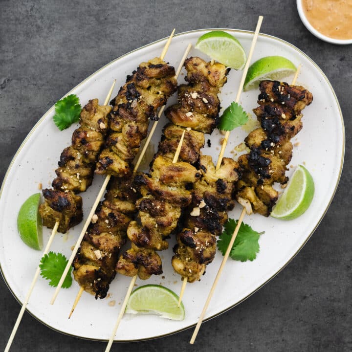 Chicken Satay served with peanut sauce on a white plate.