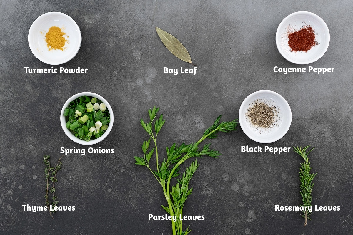 Ingredients including turmeric powder, bay leaf, cayenne pepper, spring onions, parsley leaves, black pepper powder, thyme leaves, and rosemary leaves, arranged on a surface.