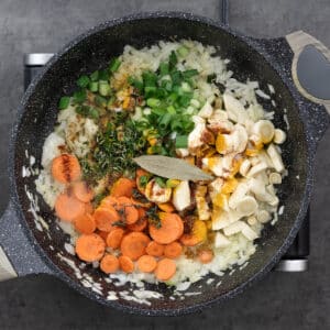 Sliced vegetables seasoned with spices and fresh herbs in a pan.