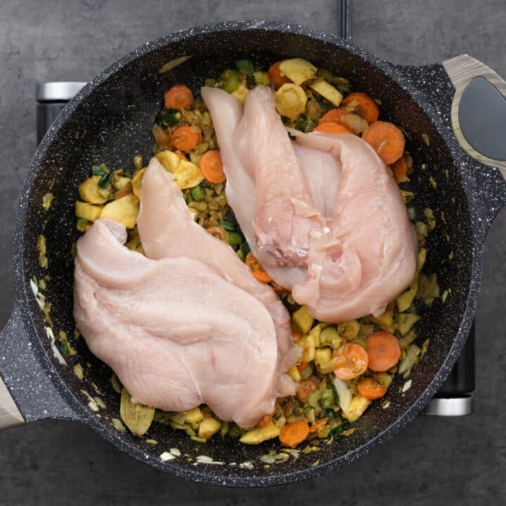 Seasoned vegetables and chicken breast in a pan.