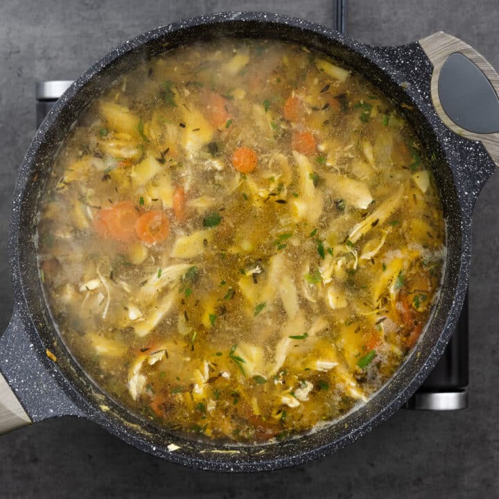 Homemade chicken soup simmering to blend the flavors in a pan.