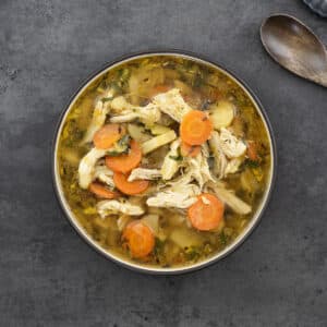 Chicken Soup served in a black bowl with a wooden spoon alongside.