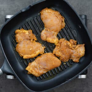 A grill pan with chicken thighs grilling.